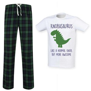 May include: A white t-shirt with the text "KNOBASAURUS" above a green dinosaur graphic. Below the graphic, the text reads "LIKE A NORMAL KNOB, BUT MORE AWESOME." Beside the shirt are green and black plaid pajama trousers with a white drawstring.