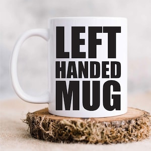 May include: White ceramic mug with black text that reads "LEFT HANDED MUG".