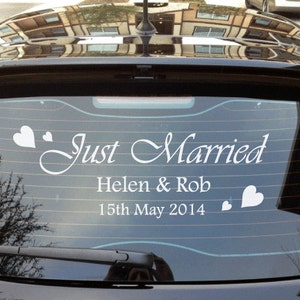 Op de afbeelding: Een witte vinyl sticker op de achterruit van een zwarte auto met de tekst "Just Married" met de namen Helen & Rob en de datum 15 mei 2014. Er zijn harten aan weerszijden van de tekst.