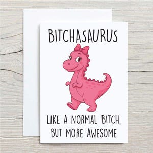 May include: A white greeting card with the text "BITCHASAURUS" above a pink cartoon dinosaur with a bow. The text below reads "LIKE A NORMAL BITCH, BUT MORE AWESOME."