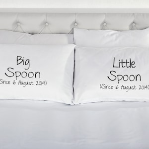 May include: Two white pillowcases with black text. The pillowcase on the left says "Big Spoon (Since 16 August 2014)". The pillowcase on the right says "Little Spoon (Since 16 August 2014)".