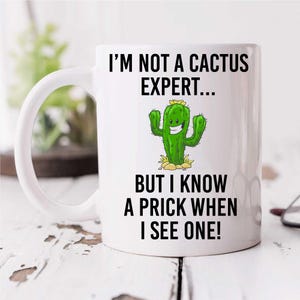 May include: White ceramic mug with a black and green cactus graphic and the text "I'm not a cactus expert... but I know a prick when I see one!"