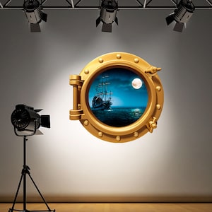 May include: A gold-coloured porthole with a view of a ship sailing on a moonlit sea. The porthole is surrounded by a dark grey wall and there are three black spotlights above.