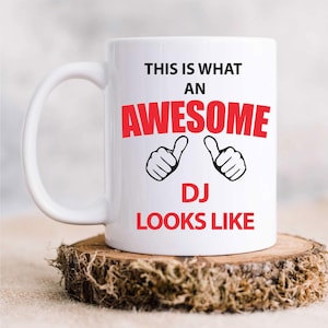 Può includere: Tazza da caffè in ceramica bianca con un design rosso e nero. La tazza dice "Questo è come appare un DJ fantastico" con due icone di pollici in su.