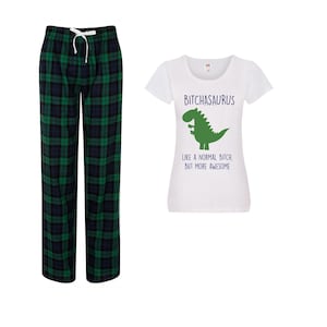 May include: A set of pajamas featuring a pair of green and navy plaid pajama pants with a white drawstring and a white t-shirt. The t-shirt has the text "BITCHASAURUS" above a green dinosaur graphic and the text "LIKE A NORMAL BITCH, BUT MORE AWESOME" below.