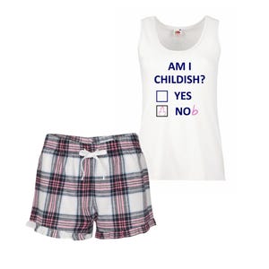 May include: A white tank top with the text "AM I CHILDISH?" and check boxes for "YES" and "NO". The "NO" box has a graphic. Plaid pajama shorts in white, black, and pink complete the set.