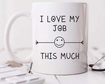 May include: White ceramic coffee mug with black text that reads "I love my job this much" with a smiley face and arrows on either side.