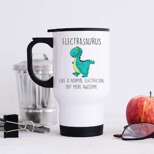 May include: White travel mug with a black lid and handle. The mug features a green cartoon dinosaur with the text "Electrasaurus like a normal electrician, but more awesome".