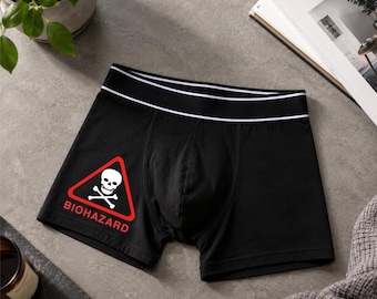 Peut inclure: Boxer noir avec une ceinture blanche et un symbole de danger biologique rouge. Le symbole de danger biologique comprend un crâne et des os croisés blancs avec le mot "BIOHAZARD" en texte rouge. Le boxer est en matière souple.