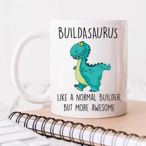 Könnte beinhalten: Eine weiße Keramiktasse mit einem grünen Comic-Dinosaurier und dem Text "BUILDASAURUS LIKE A NORMAL BUILDER BUT MORE AWESOME".