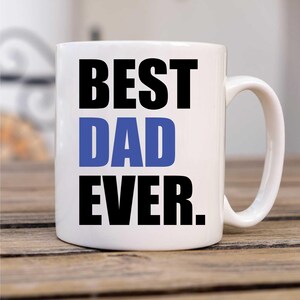 Op de afbeelding: Witte keramische koffiemok met zwarte tekst die "Best Dad Ever" zegt. Het woord "Dad" is blauw.