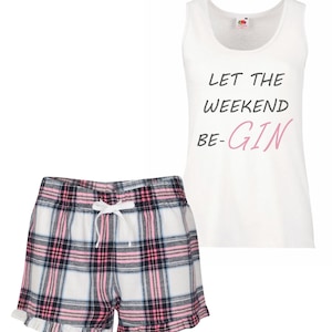 May include: White tank top with the text "LET THE WEEKEND BE-GIN" in black and pink. The set includes plaid shorts in white, pink, and black with a drawstring waist and ruffled hem. A casual sleepwear set.