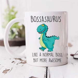 Może przedstawiać: Biały kubek ceramiczny z zielonym kreskówkowym dinozaurem i tekstem "Bossasaurus Like a normal boss, but more awesome".
