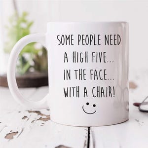 May include: White ceramic coffee mug with a black inscription that reads "Some people need a high five... in the face... with a chair!" and a smiley face.