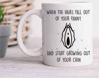 May include: White ceramic mug with a handle. The mug features black text and a black graphic of a vulva. The text reads: "WHEN THE HAIRS FALL OUT OF YOUR FANNY AND START GROWING OUT OF YOUR CHIN."