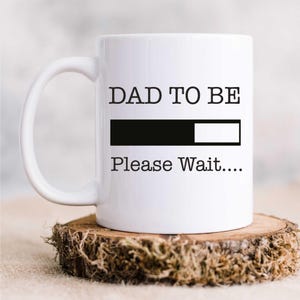 May include: White ceramic mug with a black graphic that reads "DAD TO BE" with a progress bar and the text "Please Wait..."