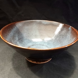 May include: A dark brown ceramic bowl with a light blue glaze. The bowl has a wide rim and a rounded base.