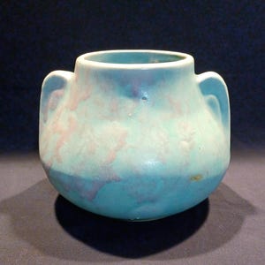 May include: A small, round ceramic vase with two handles. The vase has a turquoise base with pink and purple cloud-like patterns. The rim and handles are a lighter shade of turquoise.