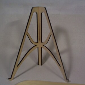 May include: A wooden display stand with a triangular base and a decorative lattice design. The stand is made of light brown wood with black accents.
