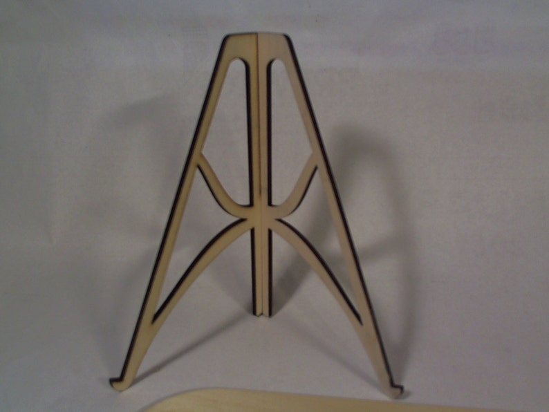 May include: A wooden display stand with a triangular base and a decorative lattice design. The stand is made of light brown wood with black accents.
