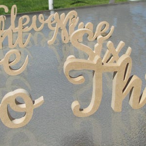 May include: Wooden numbers one through nine in a cursive font. The numbers are painted in a light brown color and are arranged on a light gray surface.