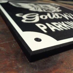 Peut inclure: Un panneau noir et blanc avec un motif d'aigle blanc et le texte "Gold Wing Parking Only". Le panneau a une bordure noire et un trou dans le coin sup&eacute;rieur droit.