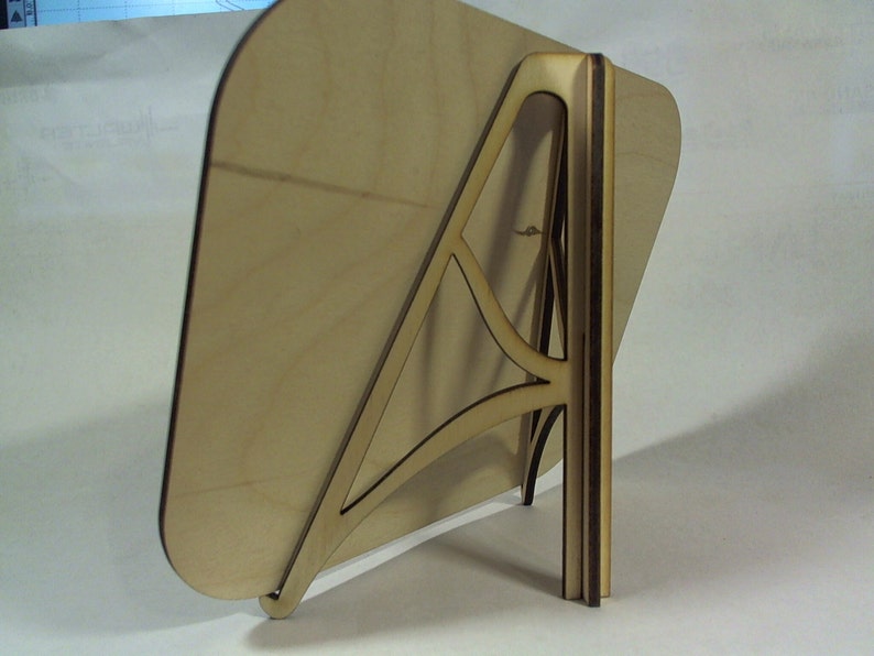 May include: A wooden easel stand with a light brown rectangular base and a dark brown support structure. The stand is designed to hold a picture or a sign.