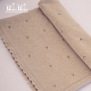 May include: A beige knitted baby blanket with a crocheted border. The blanket has a delicate pattern of small holes throughout.