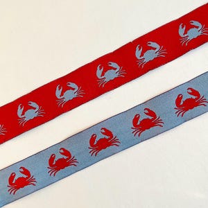 May include: Two ribbons with crab patterns. One ribbon is red with light blue crabs, and the other is light blue with red crabs. The ribbons are diagonally placed against a white background.