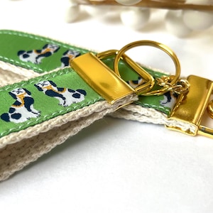 May include: A green and white key chain with a gold key ring and a gold clasp. The key chain has a pattern of black and white dogs on a green background.