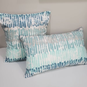 May include: Two decorative throw pillows with a blue and green abstract pattern. The pillows are made of a soft, textured fabric.