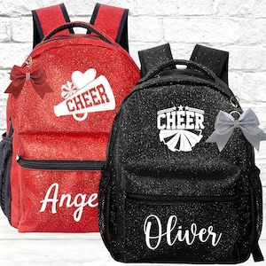 Peut inclure: Un sac à dos rouge à paillettes avec un motif de mégaphone blanc et le texte CHEER, personnalisé avec le nom Ange, et un sac à dos noir à paillettes avec un motif de mégaphone blanc et le texte CHEER, personnalisé avec le nom Oliver.