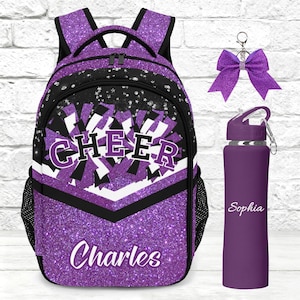 Peut inclure: Un sac à dos à paillettes violettes avec le mot CHEER et le nom Charles, accompagné d'un porte-clés nœud violet assorti et d'une gourde violette avec le nom Sophia imprimé en écriture blanche sur le côté de la bouteille.
