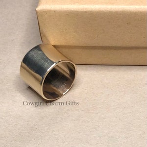 May include: A silver ring with a wide, flat band. The ring is smooth and has a polished finish. The ring is sitting on a brown surface.