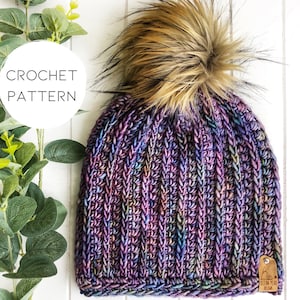 May include: A purple, blue, and green crochet beanie with a faux fur pom pom. The beanie has a tag that says "Bear & Bird Knits".