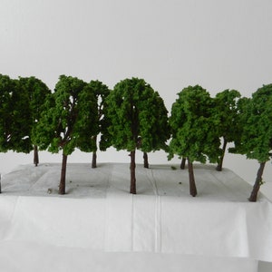 Peut inclure: Une maquette miniature d'un bosquet d'arbres. Les arbres ont des troncs bruns et un feuillage vert dense. Ils sont disposés sur une base grise, avec un fond blanc. La scène est probablement pour un train miniature ou un diorama.
