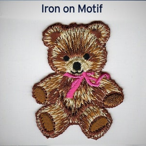 Könnte beinhalten: Bügeleisen-Motiv eines braunen Teddybären mit einem rosa Band. Der Bär hat ein gesticktes Lächeln und schwarze Augen.