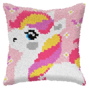 May include: A pink and white plush cushion featuring a unicorn design. The unicorn has a rainbow mane and tail, and a blue eye. The cushion is decorated with small white flowers.
