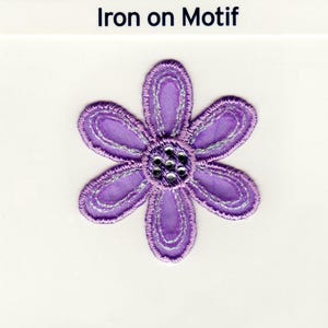 Könnte beinhalten: Lilafarbener Bügelmotiv mit einer Blüte und einem silbernen Glitzer-Zentrum.