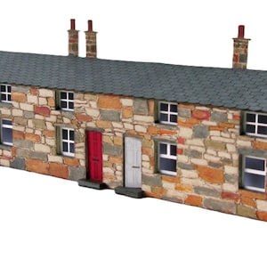 May include: A model of a row of stone cottages with a slate grey roof, chimneys, and multiple windows and doors. The doors are painted in various colours, including green, white, and red. The stone facade features a mix of brown, tan, and grey stones.