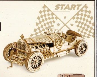 May include: A wooden model kit of a vintage race car with a checkered flag background and the word "START" printed above. The car has a number "32" on the side.