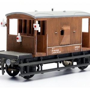 May include: A model railway caboose in brown and grey. The wooden structure has a grey roof, white signal lights, and black wheels. The model includes the text "LONDON MIDLAND" and other markings. The model is approximately 15 cm long.
