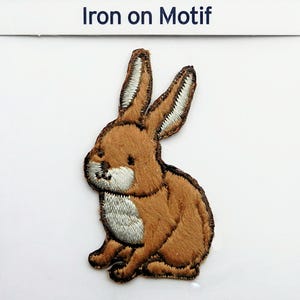 Peut inclure: Patch thermocollant brodé marron représentant un lapin assis avec des accents de fourrure blanche autour du visage et de la poitrine.