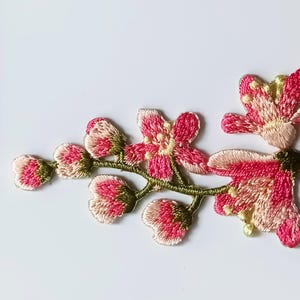 May include: Pink and green embroidered iron-on motif of a delicate flower branch. "Iron on Motif" is written on the white background.