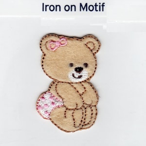 Può includere: Motivo da stirare di un orsacchiotto marrone con un fiocco rosa e un pannolino a pois rosa e bianchi.