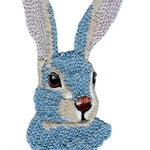 May include: Embroidered patch of a blue rabbit's head with white fur and brown eyes.