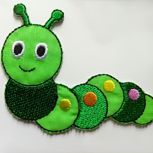 May include: Green felt caterpillar applique with a smiling face, two white eyes, and a black mouth. The caterpillar has six segments with colorful circles on each segment.