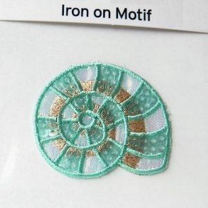May include: A turquoise and gold iron-on motif of a seashell with sequins. "Iron on Motif" is written on the white background.