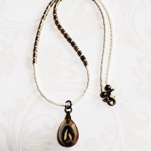 May include: A white and gold beaded necklace with a brown and white shell pendant. The pendant has a leaf design.