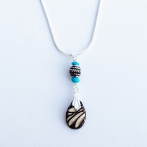 May include: A silver chain necklace with a turquoise and silver bead pendant and a brown and white patterned pendant.